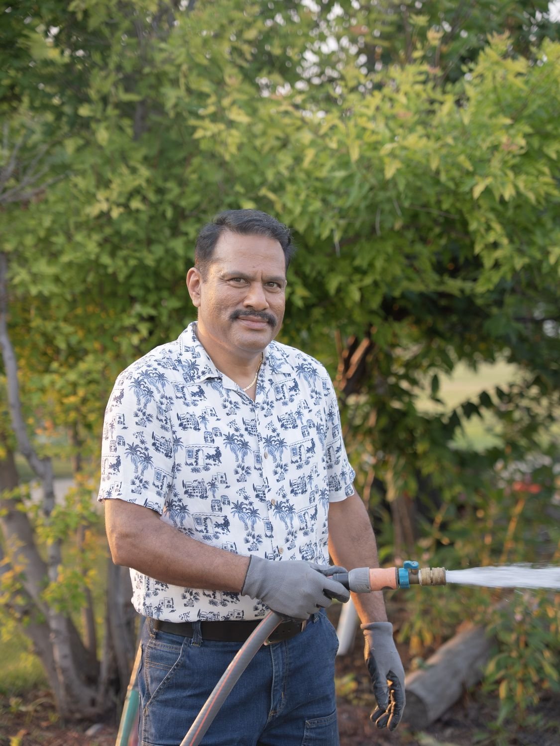 Jacky Maan in his garden, holding a running hose